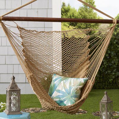 a hammock hanging from the side of a house with pillows and lanterns on the grass