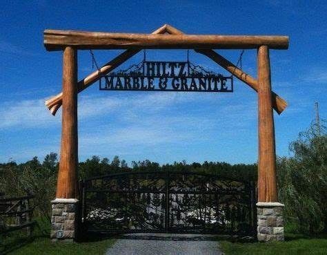 a large wooden sign hanging from the side of a metal and wood gate in front of a lush green field