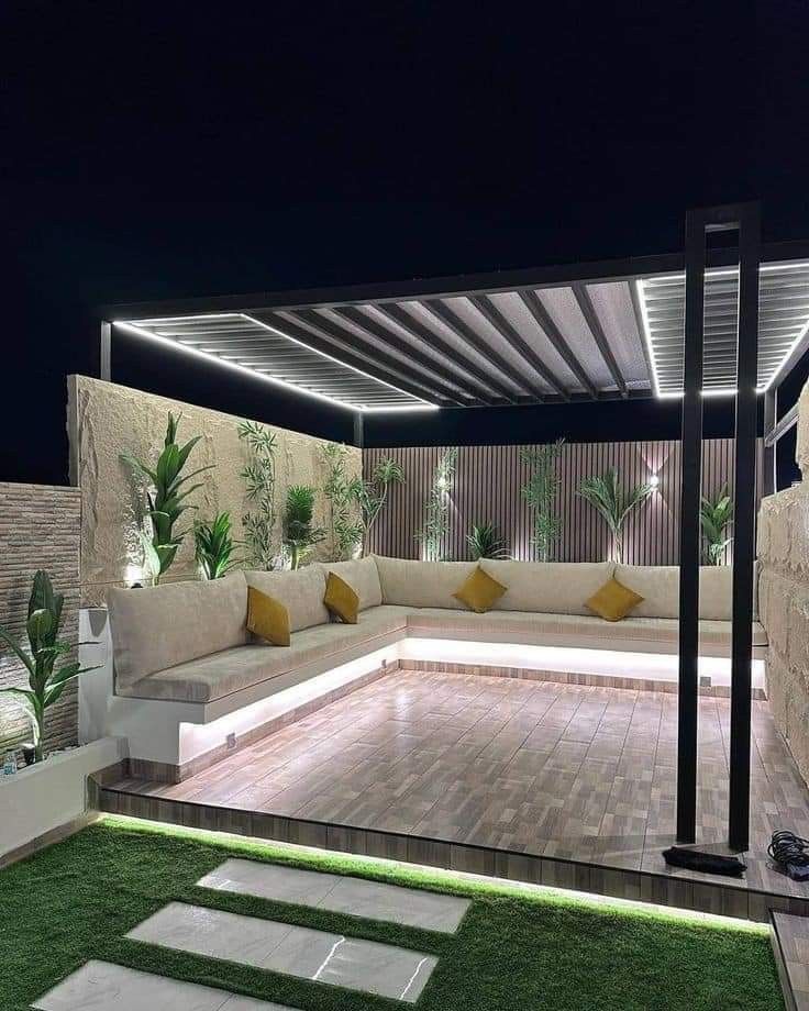 an outdoor living area at night with white couches and green grass on the ground