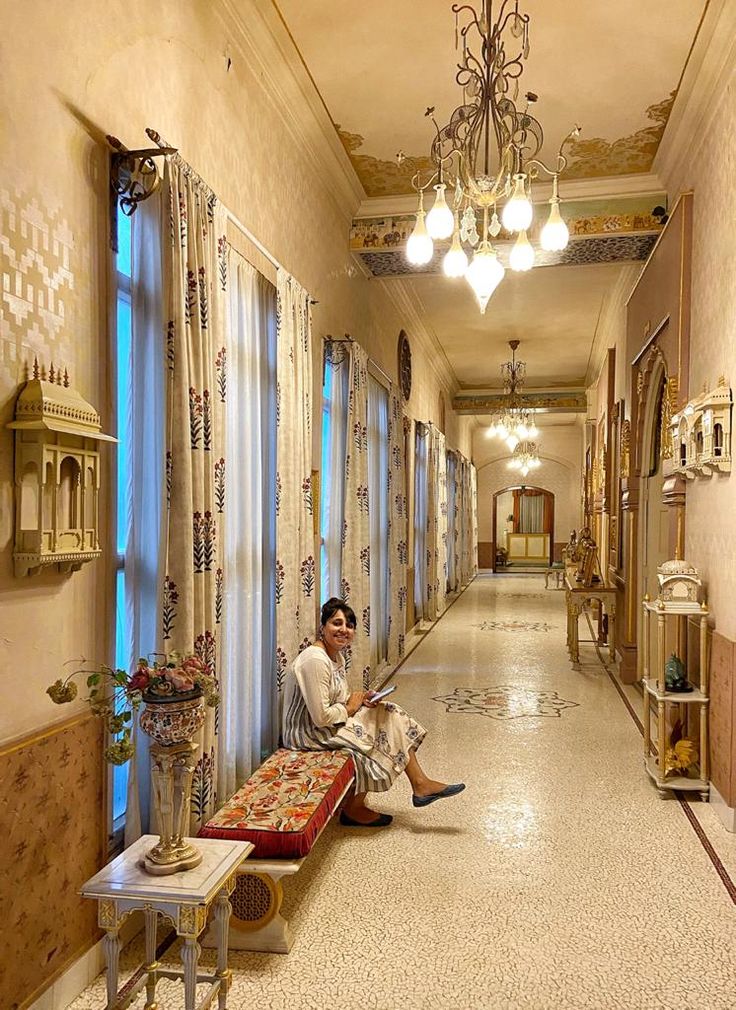 a person sitting on the floor in a hallway with curtains and windows, looking at a tabletop