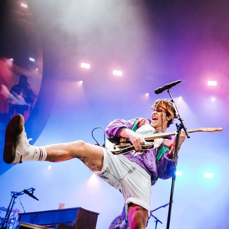 a man is performing on stage with his legs in the air while holding a guitar