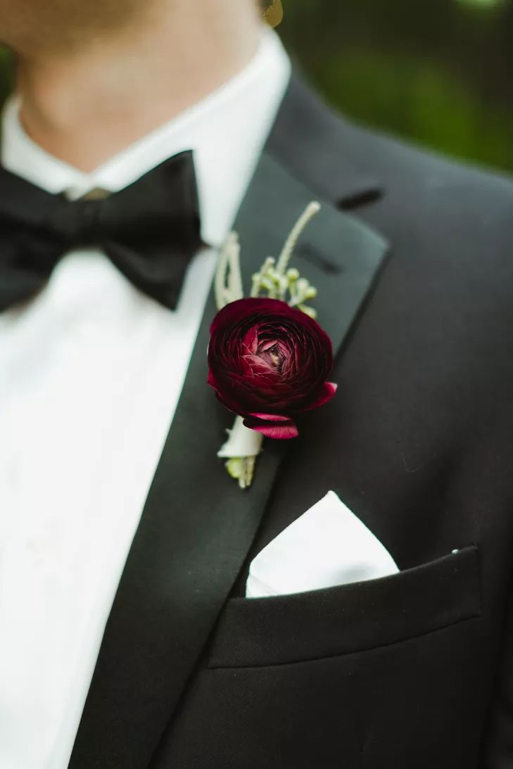 a man wearing a black tuxedo with a red flower on it's lapel