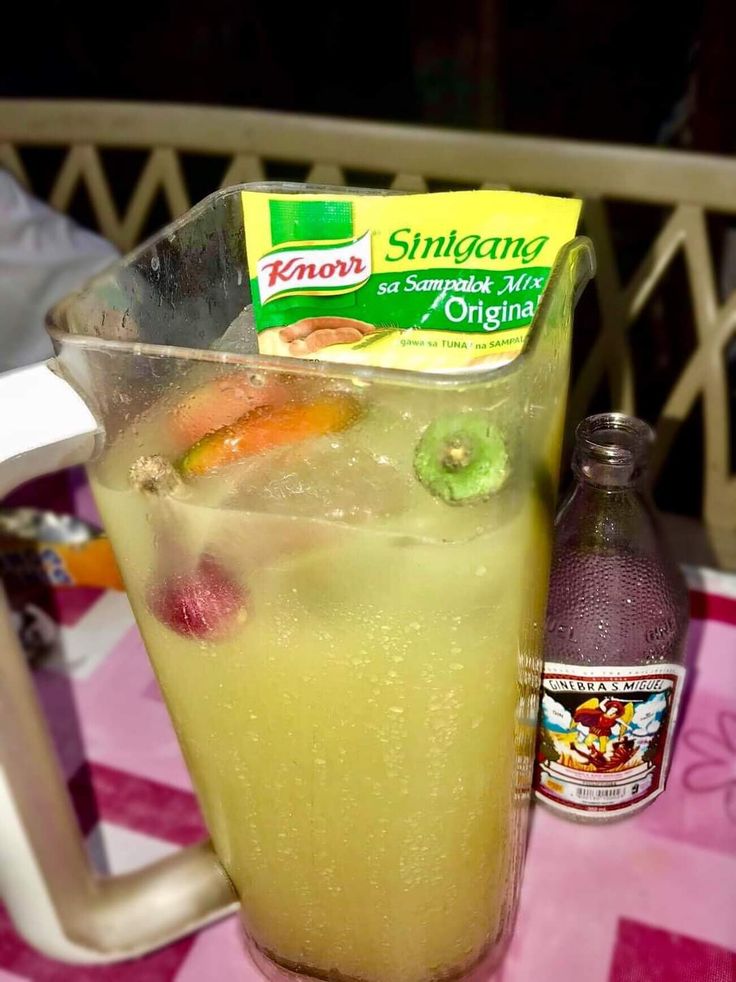 a pitcher filled with liquid sitting on top of a table next to a soda bottle