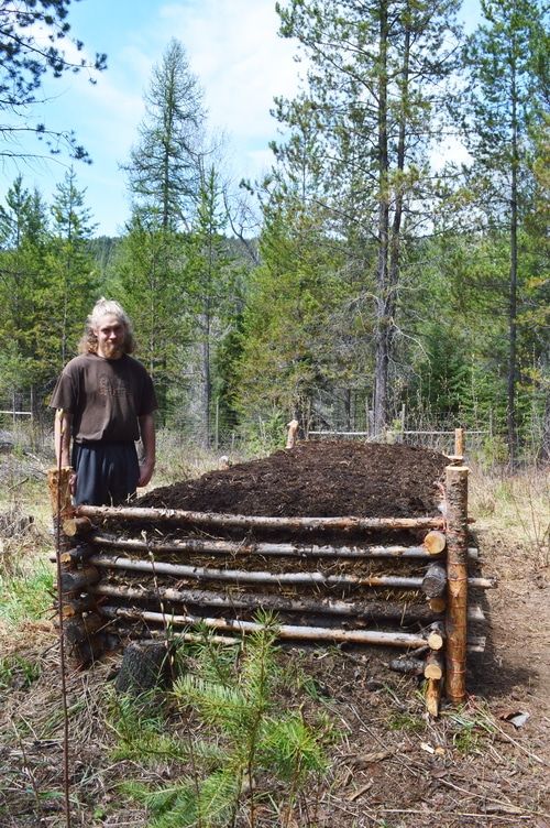 a man standing next to a pile of dirt in front of a fence made of logs