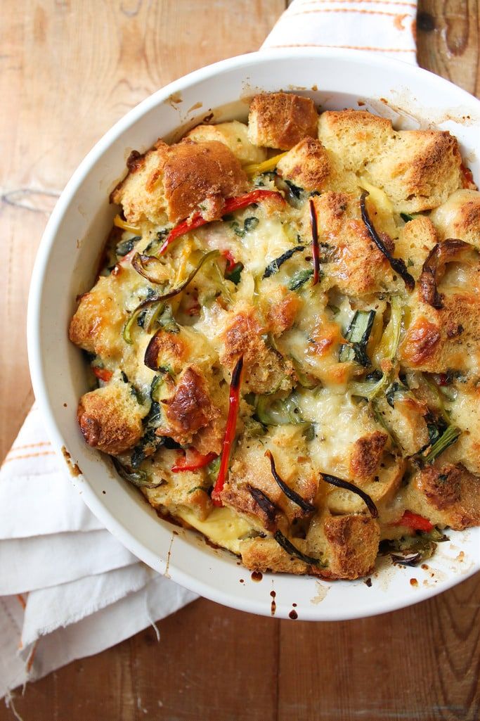 a casserole dish with bread and vegetables in it sitting on a wooden table