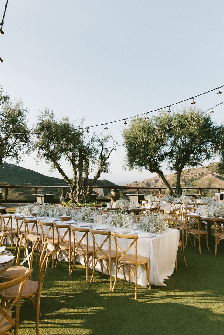 tables and chairs are set up for an outdoor wedding reception with string lights strung from the trees