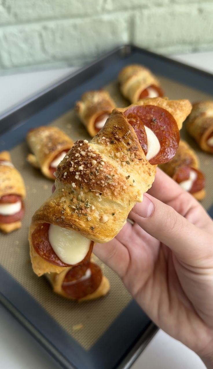 a person holding up a piece of bread with pepperoni and cheese on it