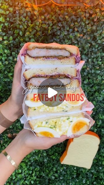 someone holding up some sandwiches with eggs and ham on them in front of green bushes