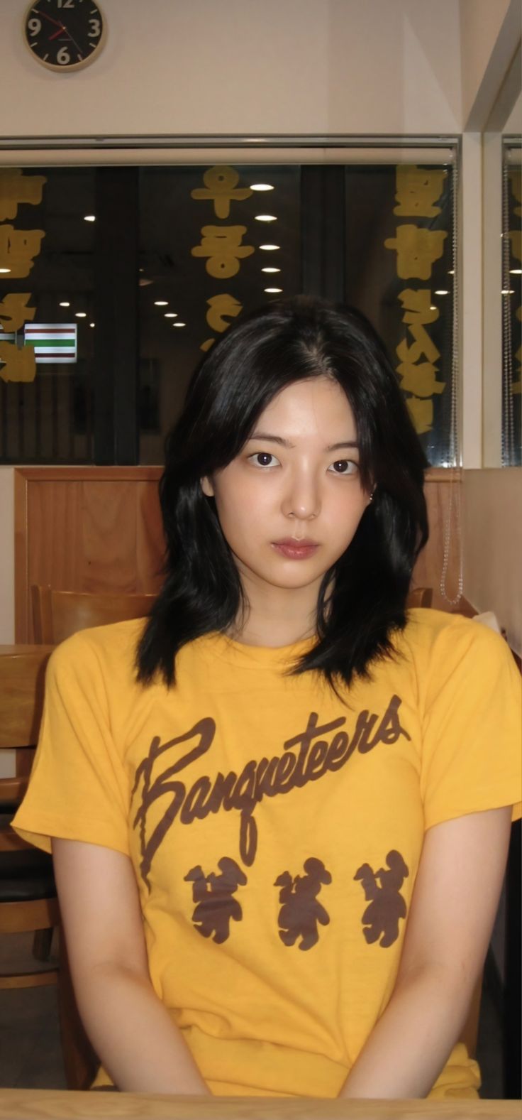 a young woman sitting at a table in front of a clock