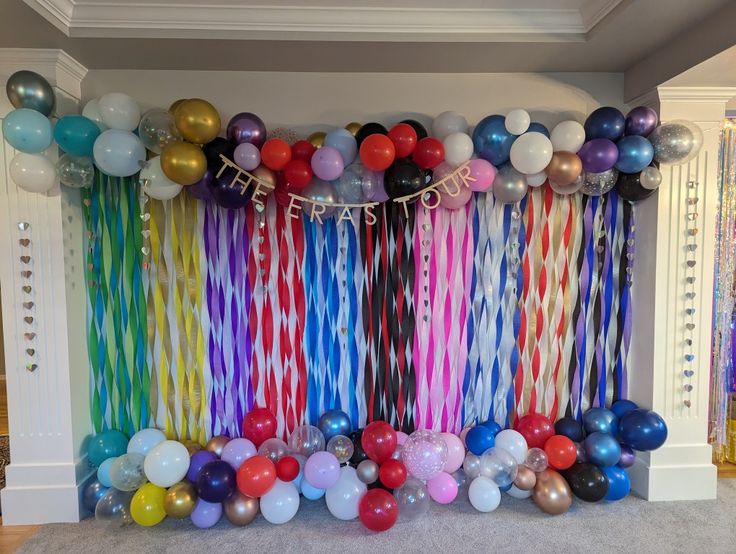 balloons and streamers are hanging from the wall in front of a party backdrop that is multicolored