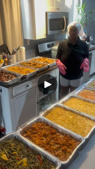 a woman standing in front of a counter filled with trays of different types of food