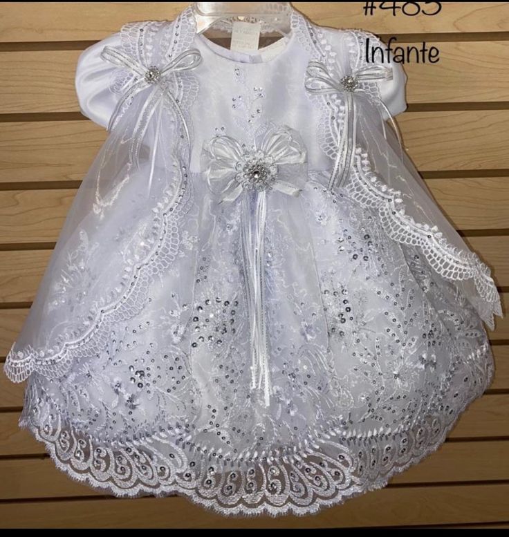 a white dress with bows on the back and lace trimmings is hanging from a hanger