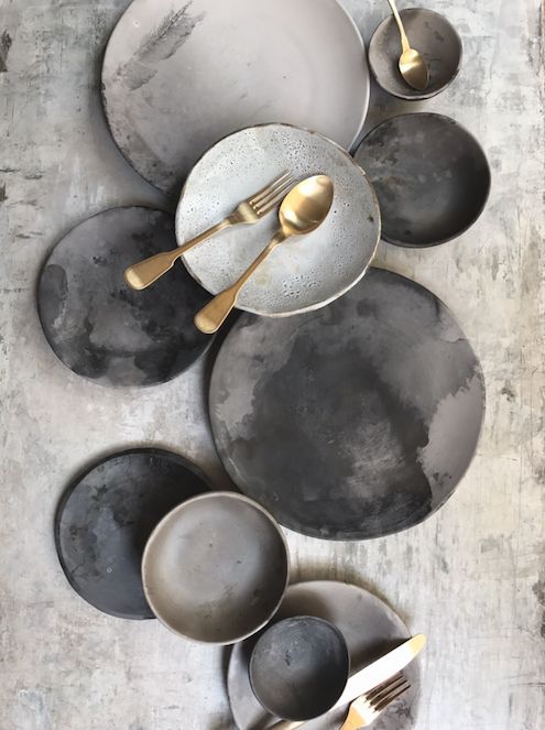 the table is set with black and white plates, silverware and gold utensils