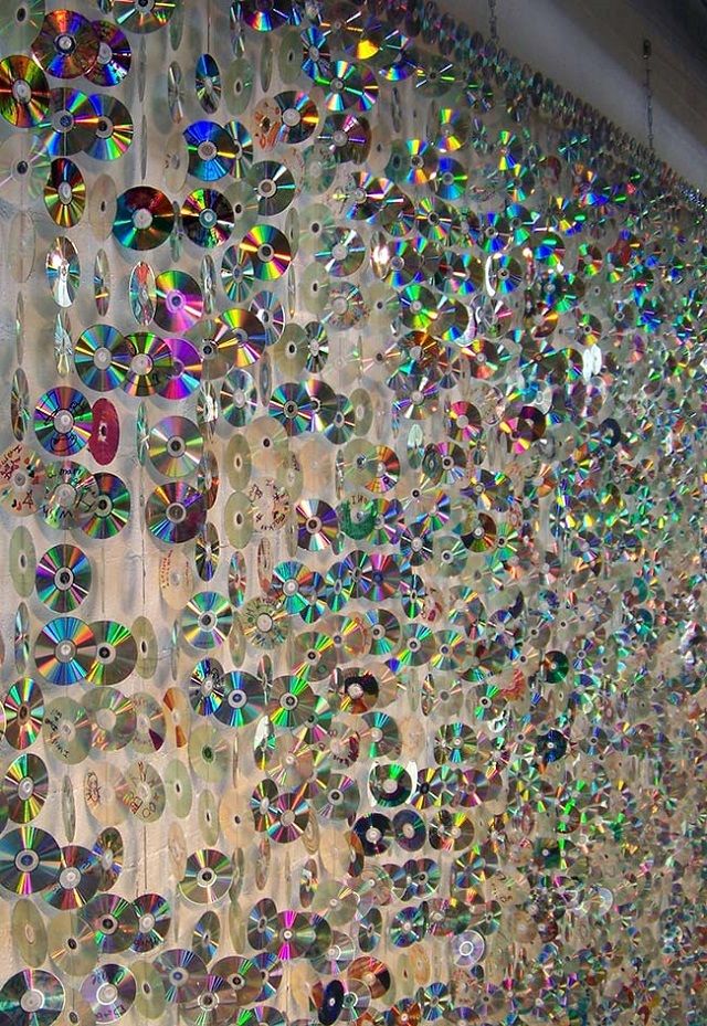 many cds are hanging on the wall in front of a window with iridescent colors