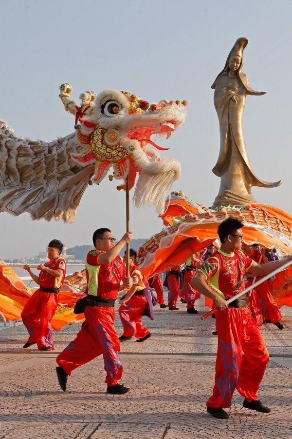 some people in red and orange outfits are dancing with dragon heads on their head as they walk down the street