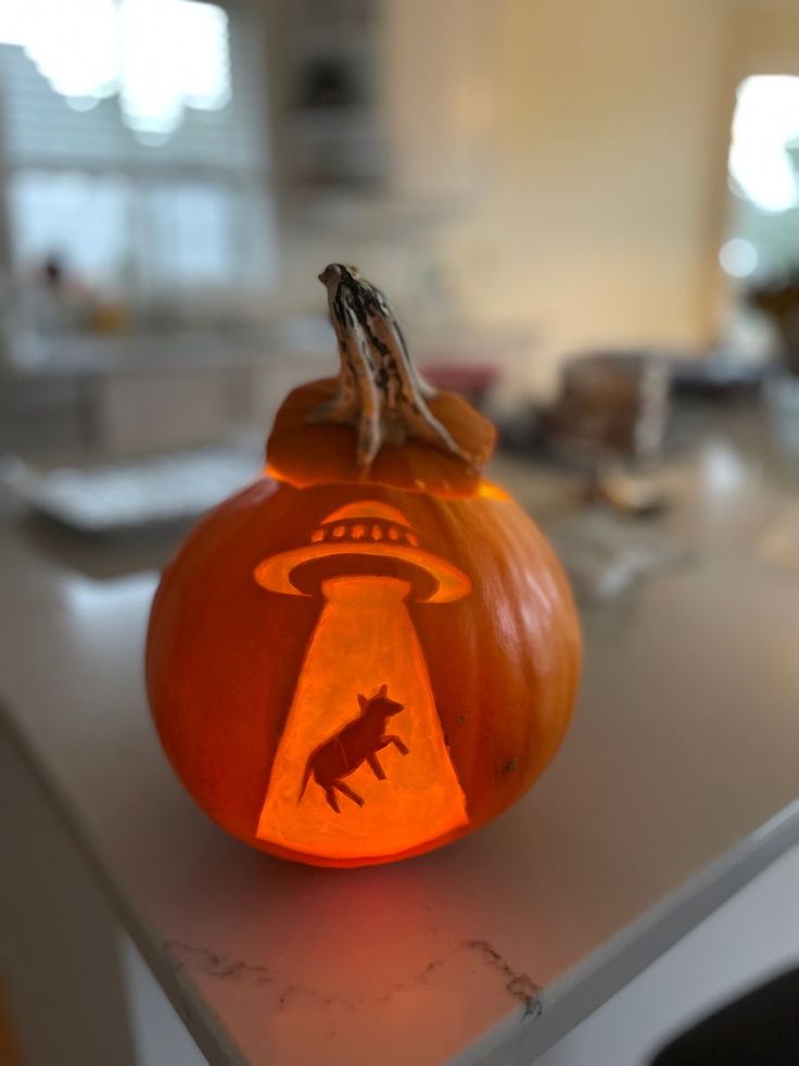 a carved pumpkin with an alien on it sitting on a counter top in a kitchen