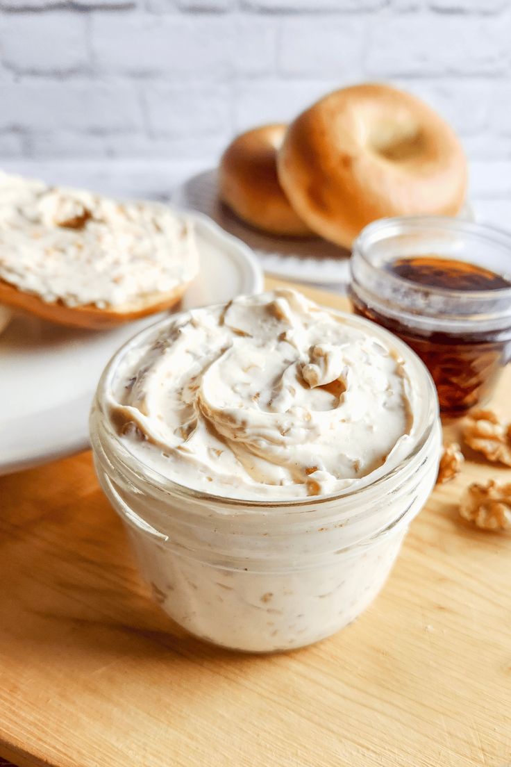 a bowl of whipped cream sitting on top of a wooden cutting board next to bagels