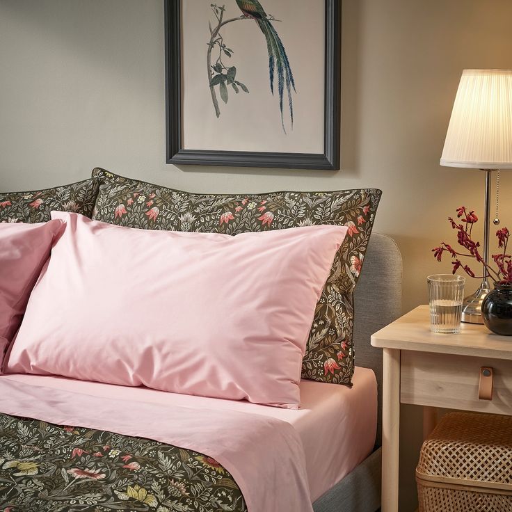 a bed with pink sheets and pillows on top of it next to a nightstand table