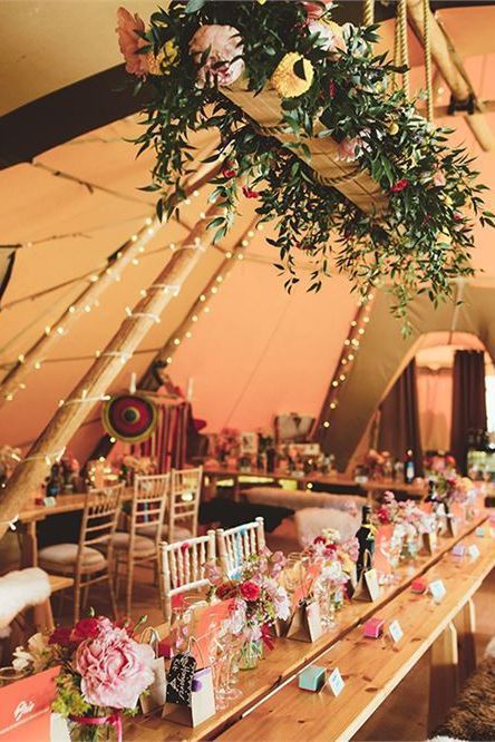 the tables are set up for a wedding reception in a tent with lights and greenery hanging from the ceiling