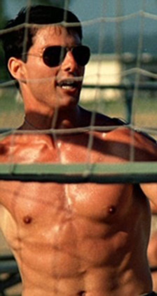 a man with no shirt on standing in front of a soccer net wearing sunglasses and holding a tennis racquet