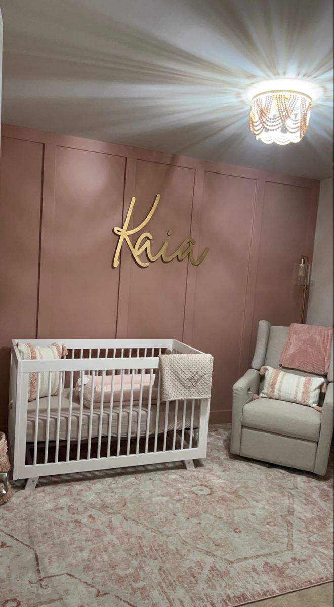 a baby's room with a crib, chair and name sign on the wall