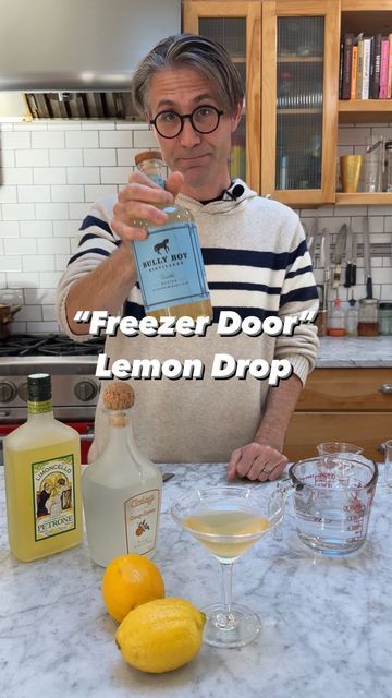 a man holding a bottle of lemon drop in front of a counter top with bottles and glasses on it