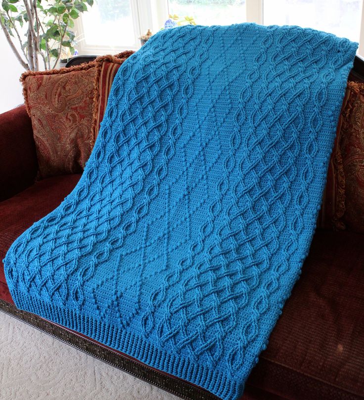 a blue knitted blanket sitting on top of a couch