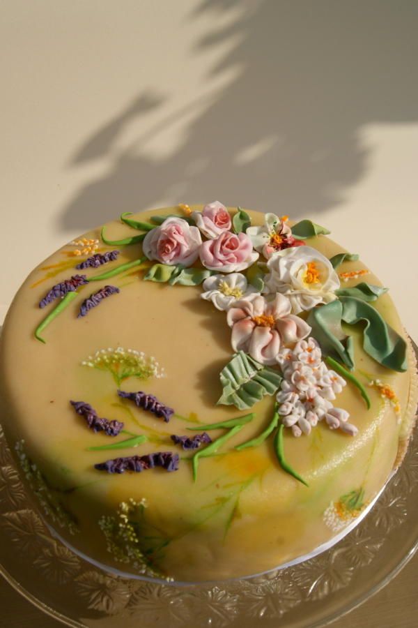 a cake with flowers on it sitting on a glass plate next to a shadow of a person