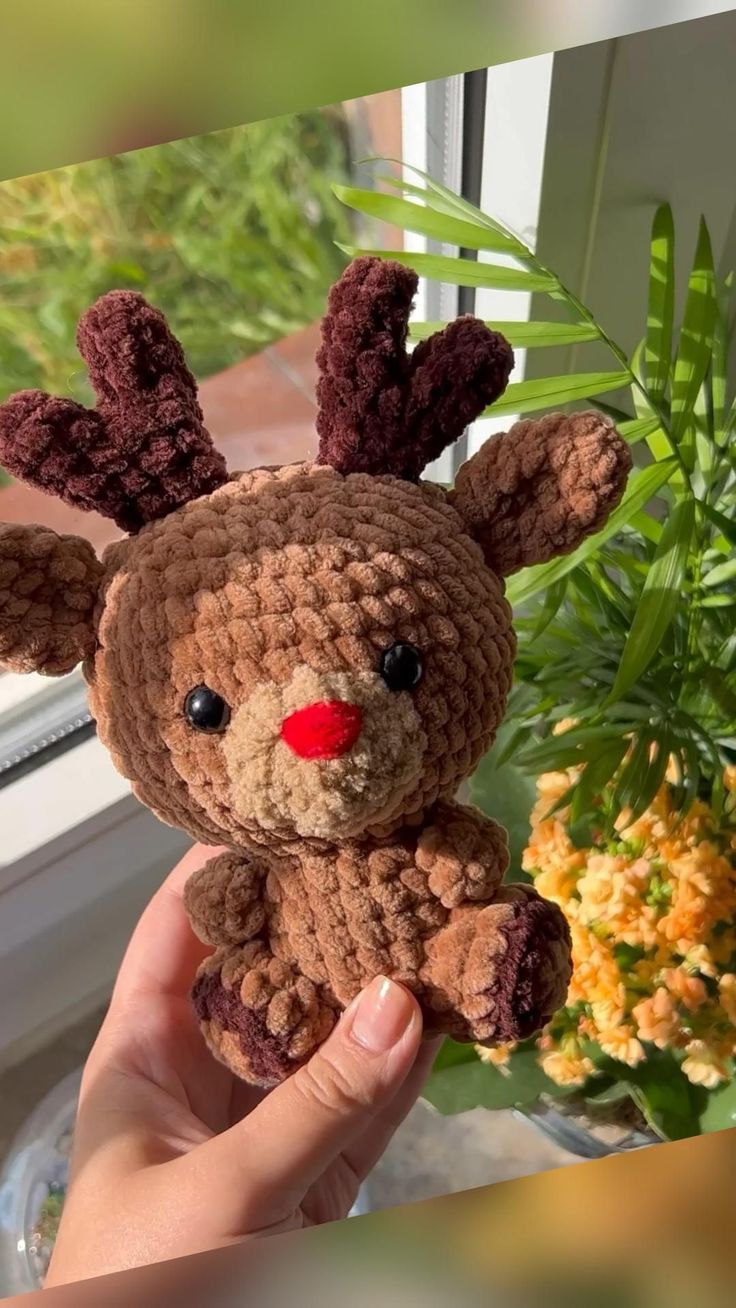 a hand holding a small crocheted stuffed animal in front of a potted plant