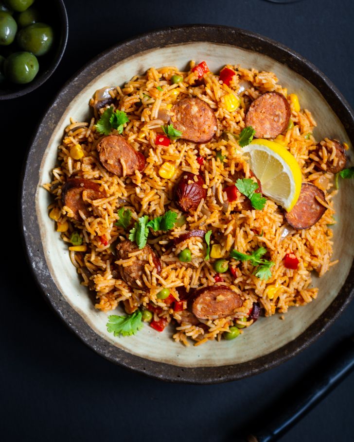 a plate full of rice, sausage and olives next to some green olives