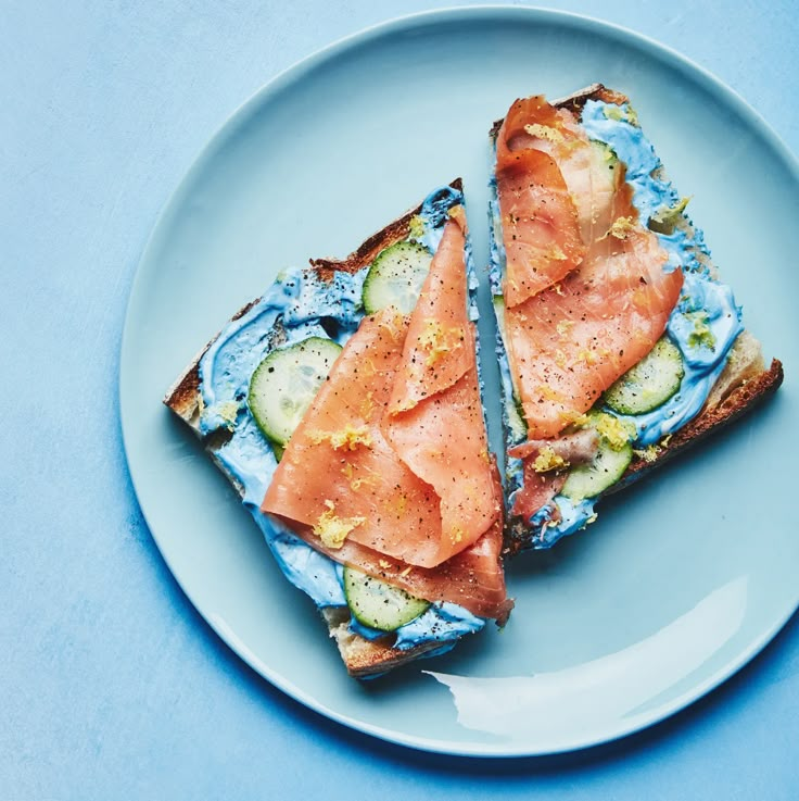 there is a sandwich with cucumbers and salmon on the blue plate next to it