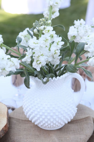 a white vase filled with flowers sitting on top of a wooden table next to a piece of wood