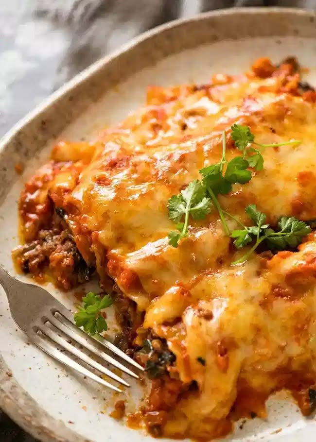 a white plate topped with lasagna covered in sauce and cheese next to a fork