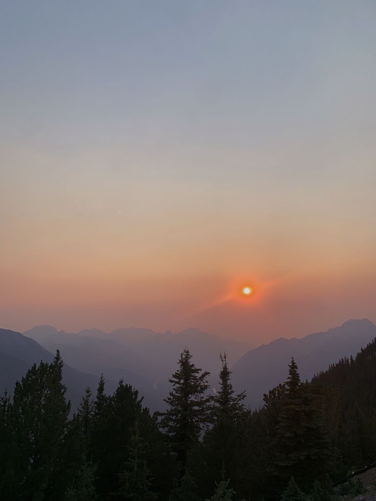 the sun is setting over some mountains and trees