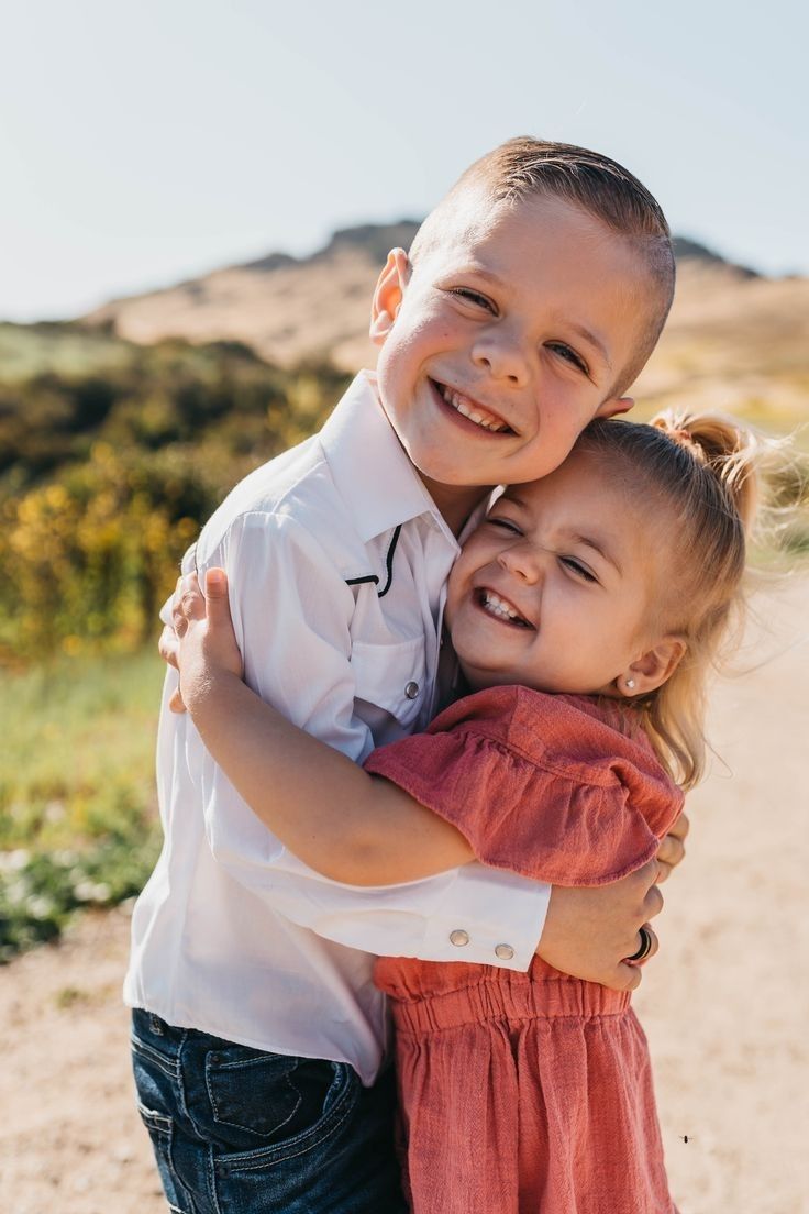 two young children are hugging each other on the dirt road in front of some hills