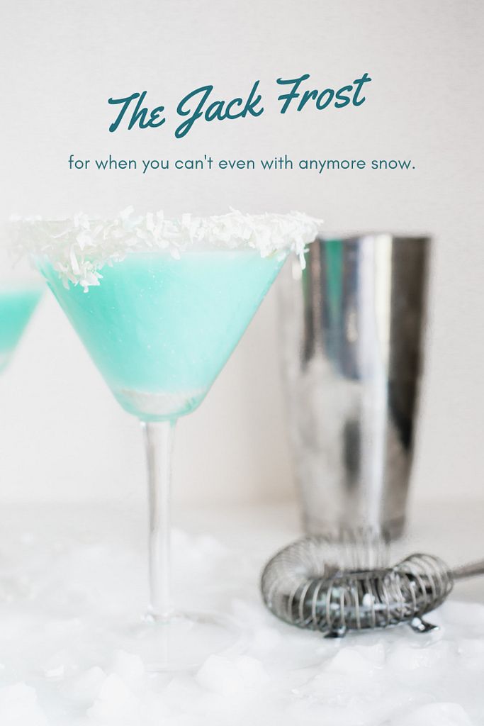 two martini glasses filled with blue liquid and white flakes on a table next to a cocktail shaker