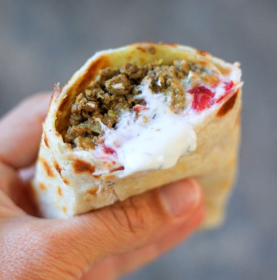 a hand holding a burrito filled with meat, cheese and sour cream on top