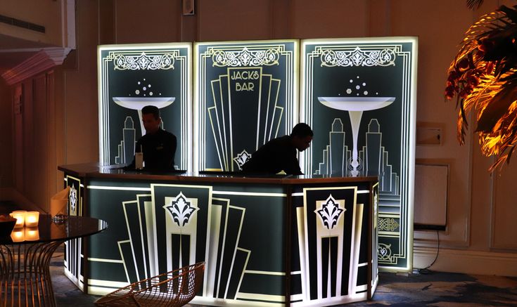 two men are standing at the front desk of a hotel lobby with art deco decor