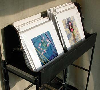 two paintings are sitting on top of a black stand with metal bars holding them up against the wall