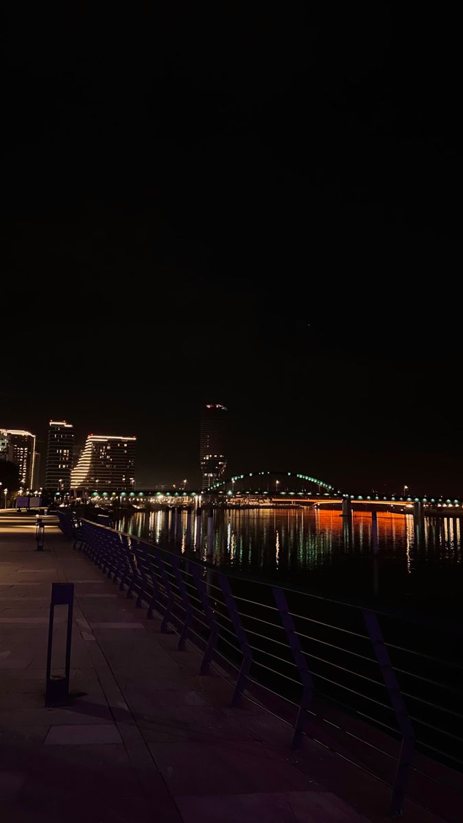 the city skyline is lit up at night with lights reflecting on the water and buildings in the background