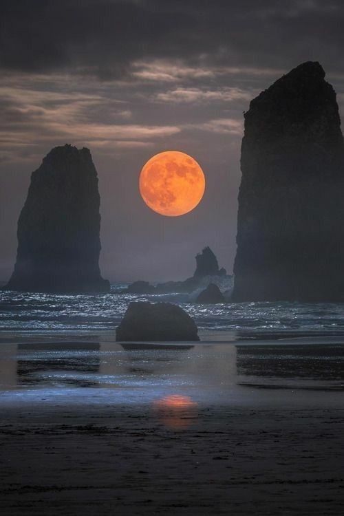 the full moon is setting over some rocks in the ocean with an orange light on them