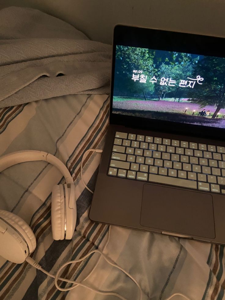 an open laptop computer sitting on top of a bed next to headphones and a blanket