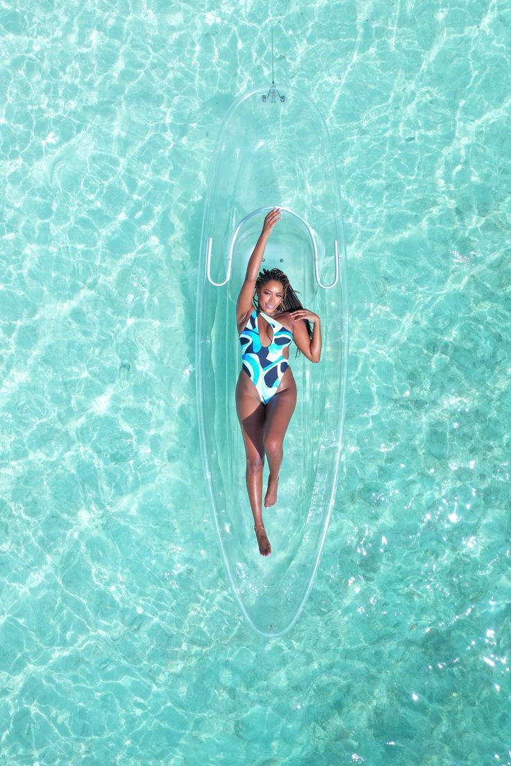 a woman in a white and blue swimsuit floating on a clear water raft with her arms up