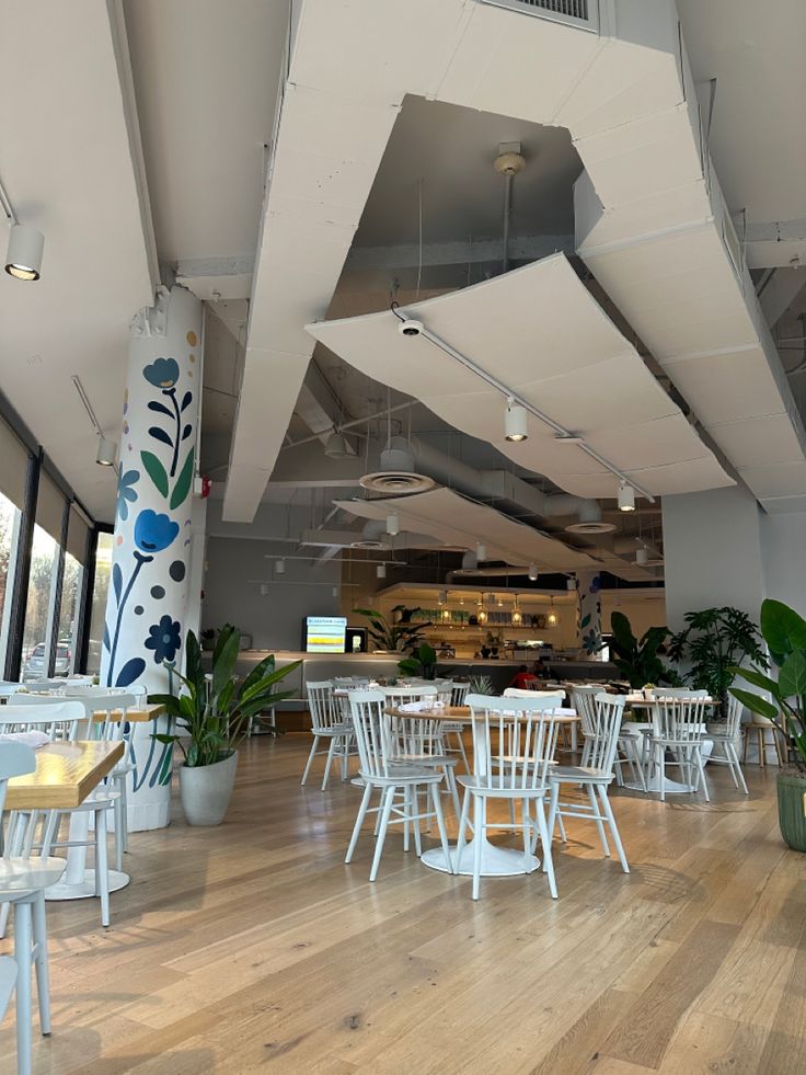 the inside of a restaurant with tables and chairs, potted plants and large windows