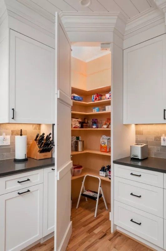 an open pantry with white cabinets and black counter tops in a home kitchen, along with wooden flooring