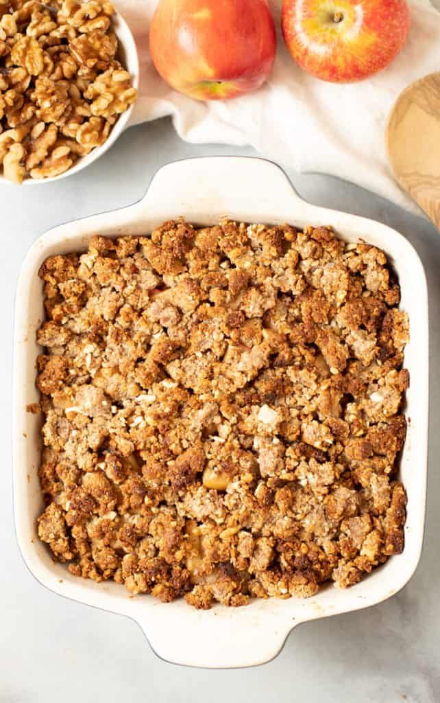 an apple crisp in a white casserole dish next to two apples