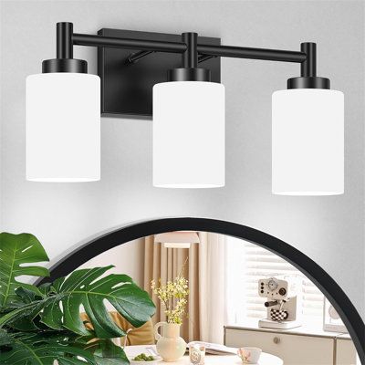 three light bathroom fixture with black finish and white glass shades on the top, along with a potted plant