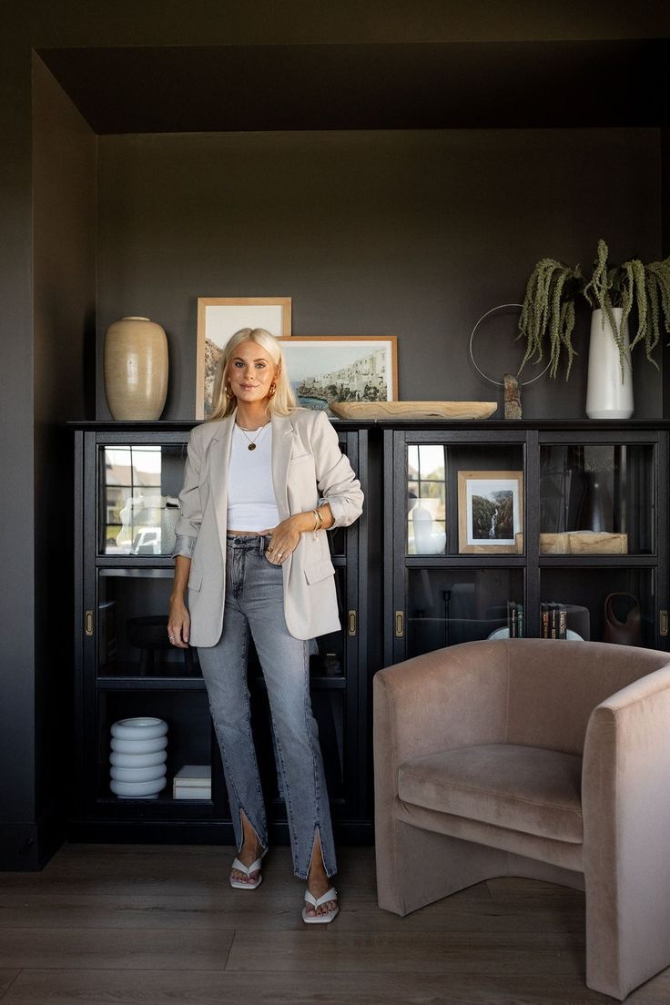 a woman standing in front of a black bookcase with pictures on the wall behind her