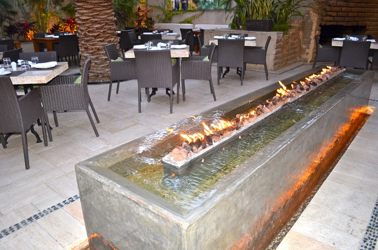 an outdoor dining area with tables, chairs and a large fire pit in the center