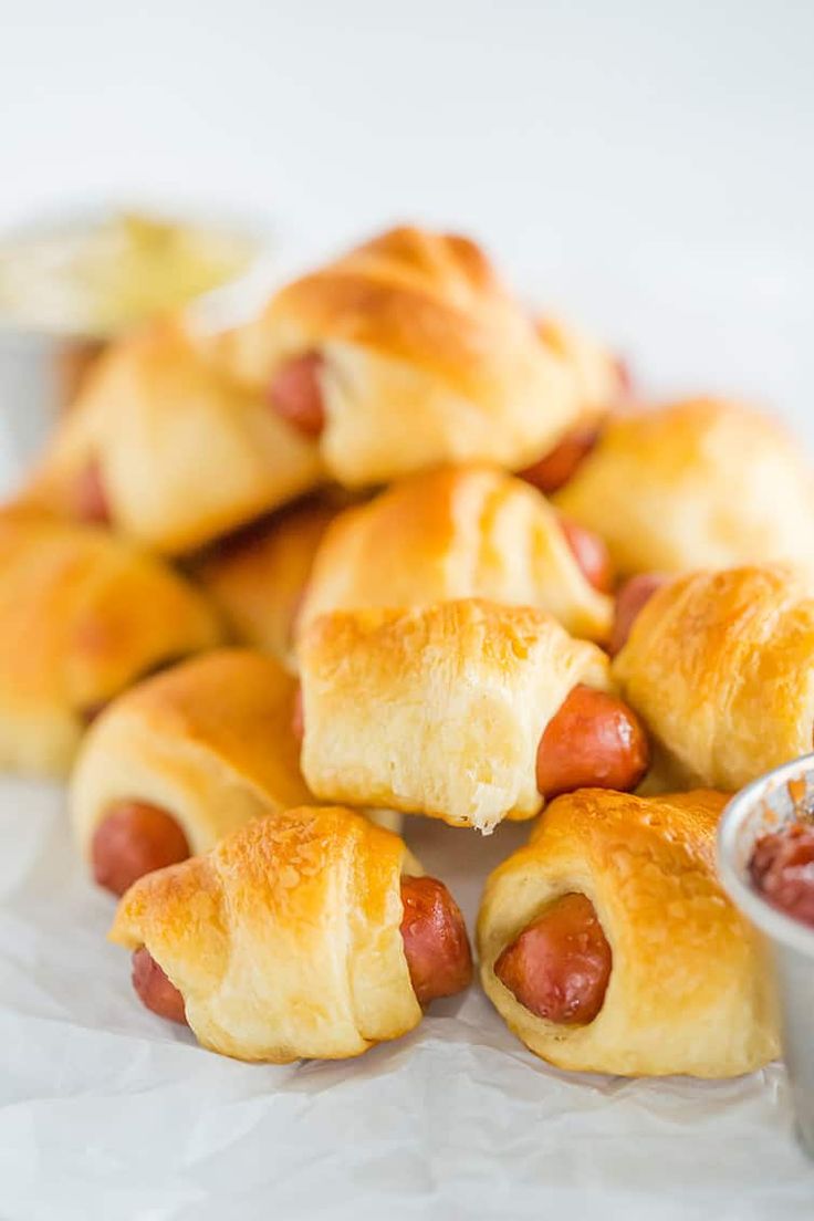 hotdogs wrapped in crescent rolls with ketchup and dipping sauce on the side